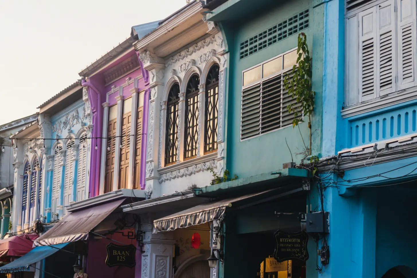 Row of colorful Sino-Portuguese shophouses with intricate window details in Phuket Old Town