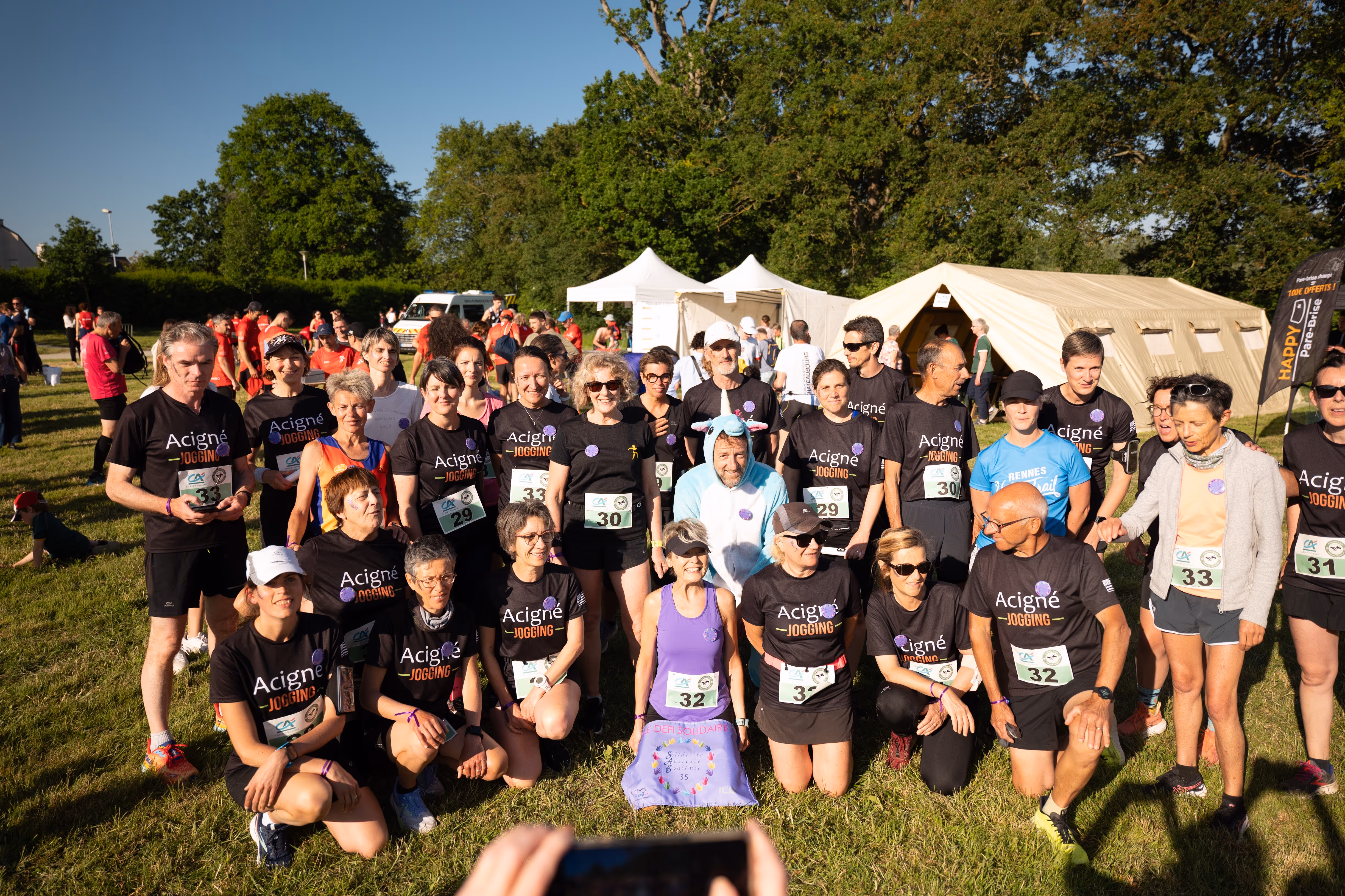 Groupe de coureurs et marcheurs portant des t-shirts noirs "Acigné Jogging" posant pour une photo en plein air lors d'un événement sportif.