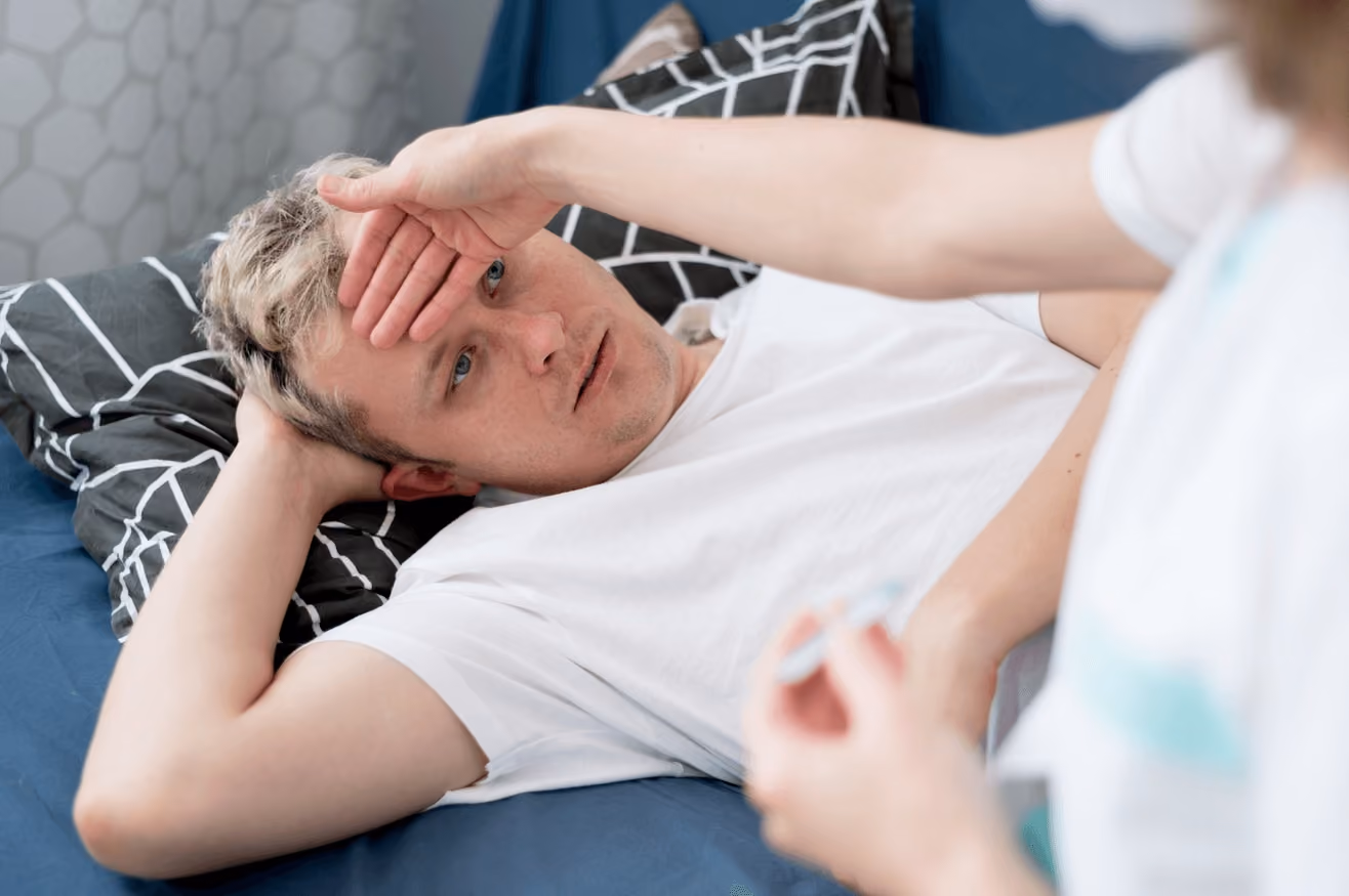 Man lying in bed with a severe headache, perhaps from a cavernous malformation, highlighting the need for evaluation by the best neurosurgeon in Los Angeles.