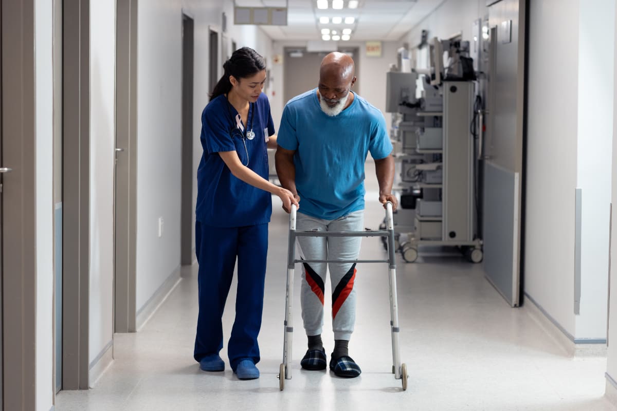 Patient recovering from spinal fusion surgery walks with a nurse and mobility aid, highlighting care from the best spine surgeon in Santa Barbara, CA.