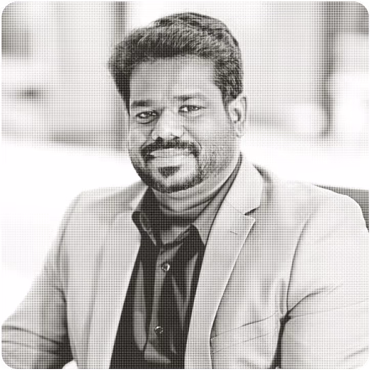 Portrait of a smiling man with short hair and beard wearing a blazer and dark shirt.