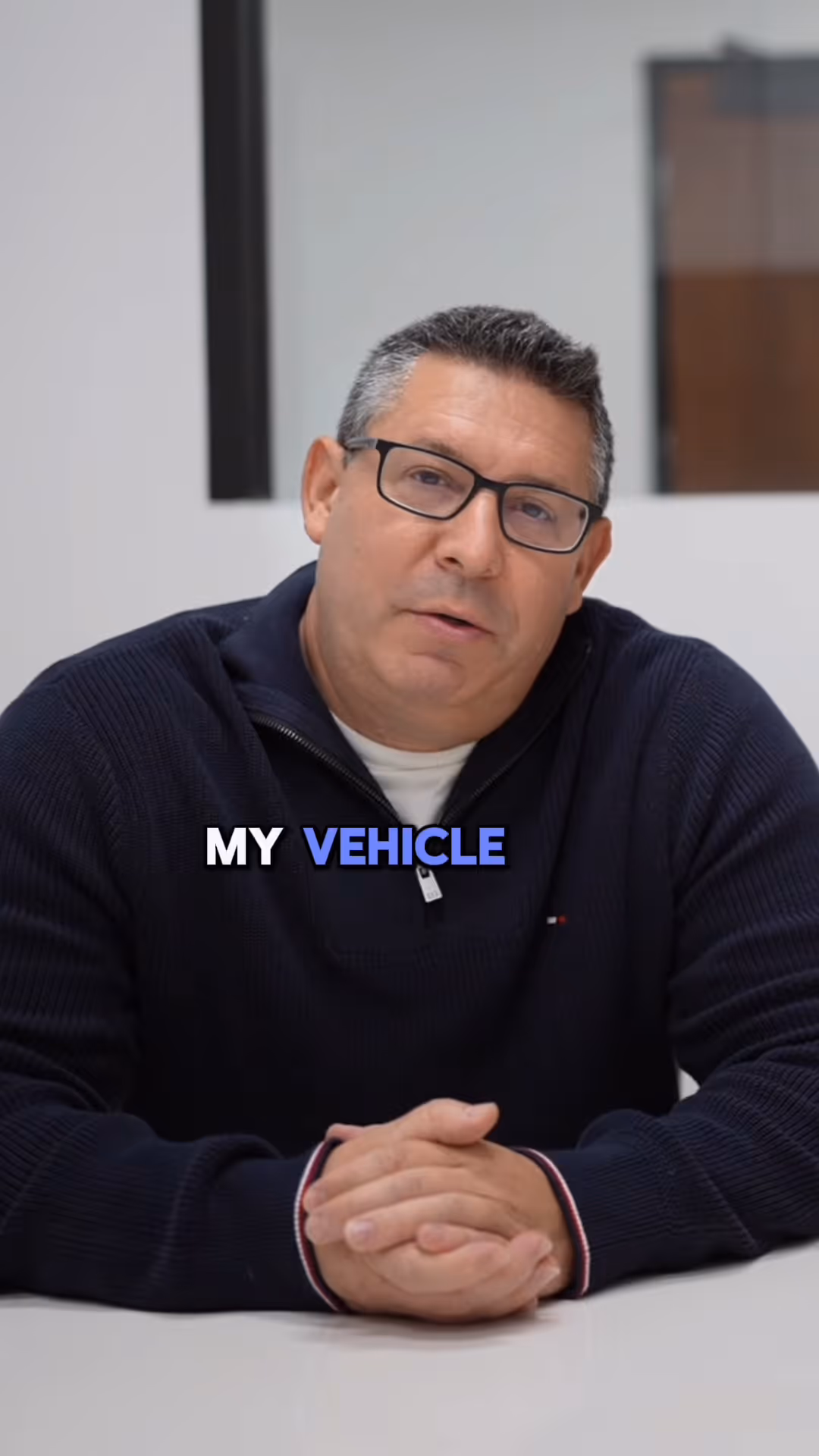 Man with glasses wearing dark sweater sits at table with text 'MY VEHICLE' in front.