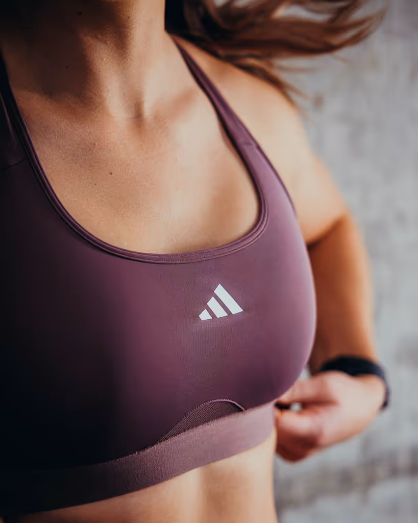Close-up of a woman adjusting her purple Adidas sports bra while exercising.