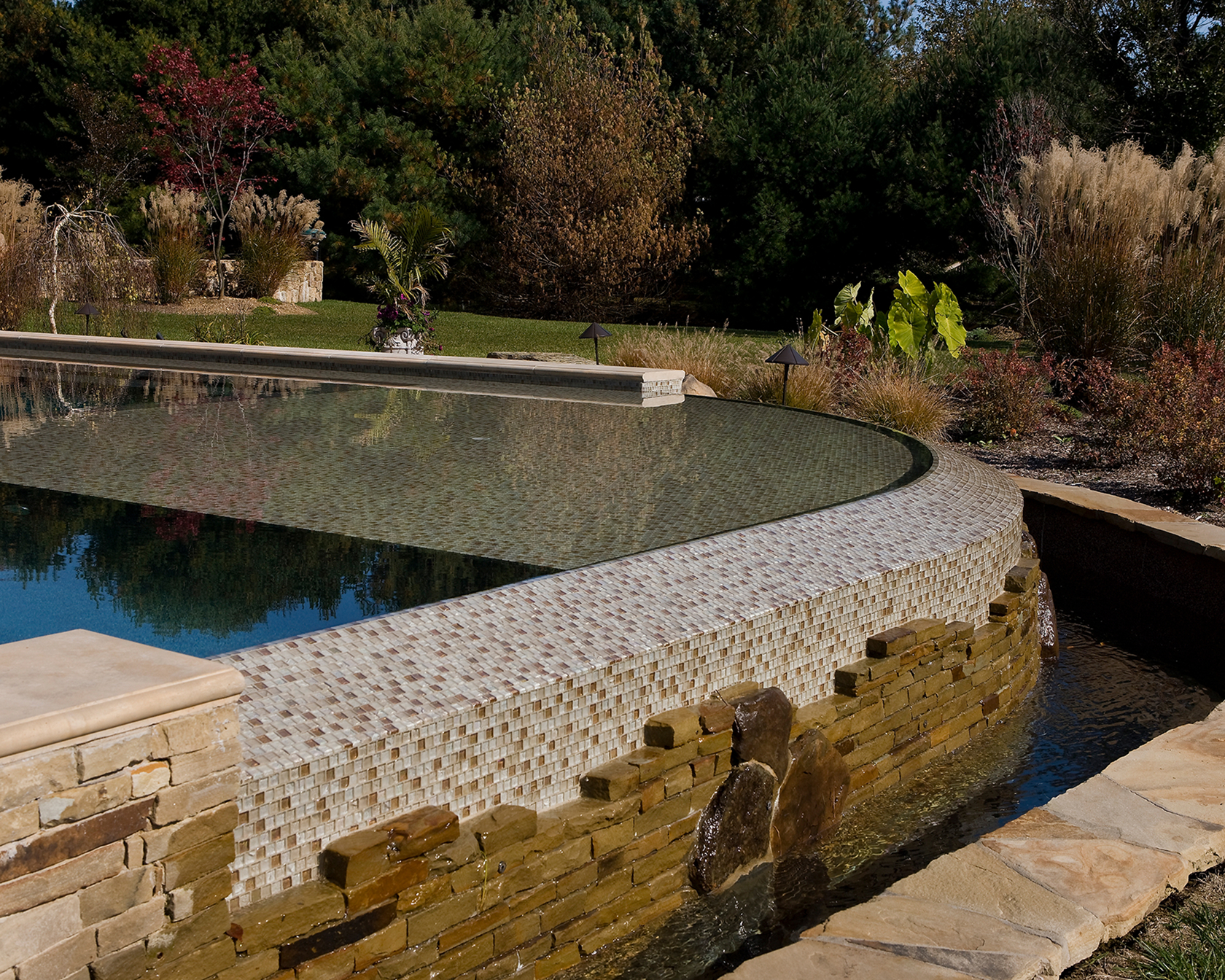 Warm decking and raised stone planters blending the pool with the natural meadow