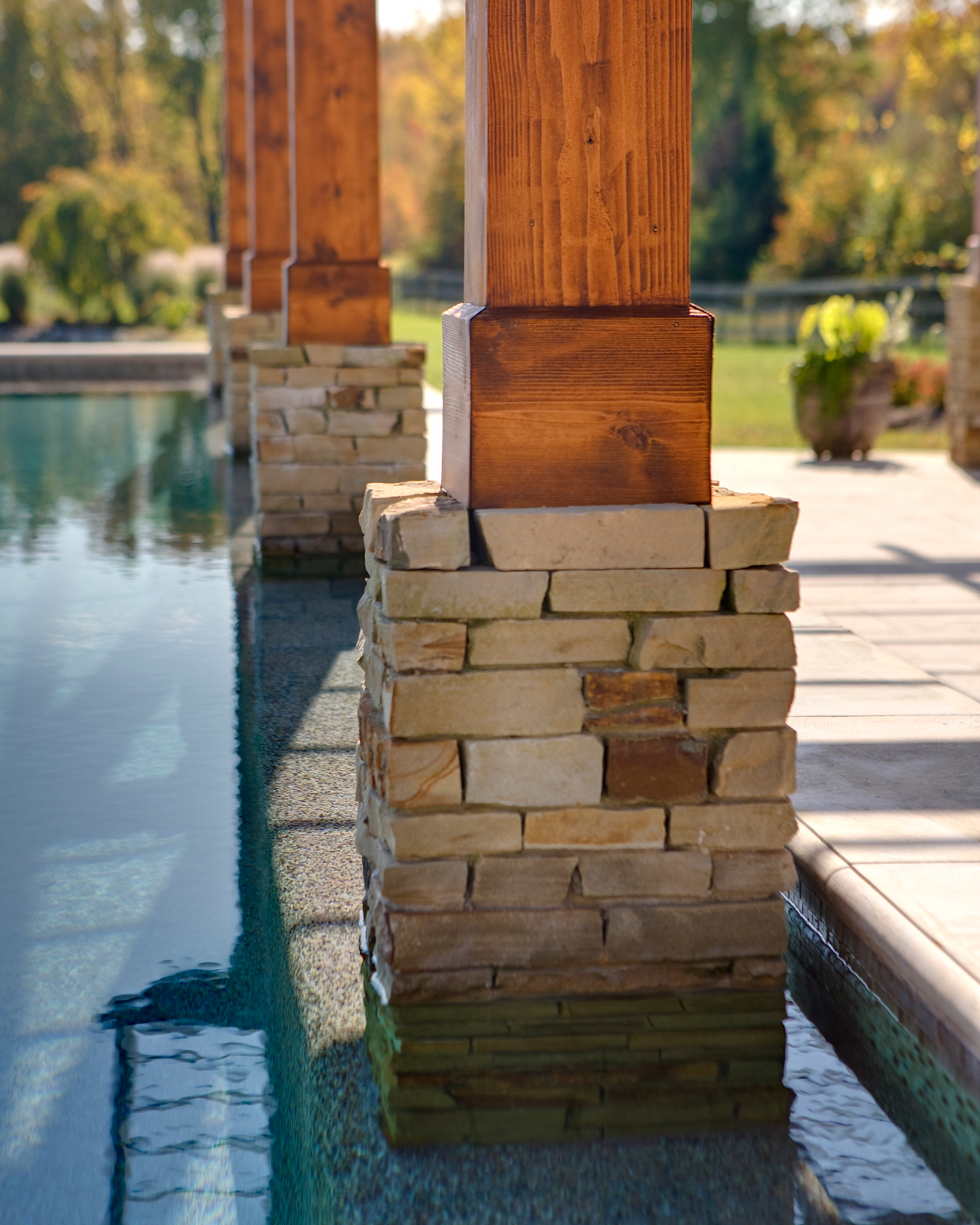 Wood pergola with stone columns beside a calm, glassy reflecting pool.