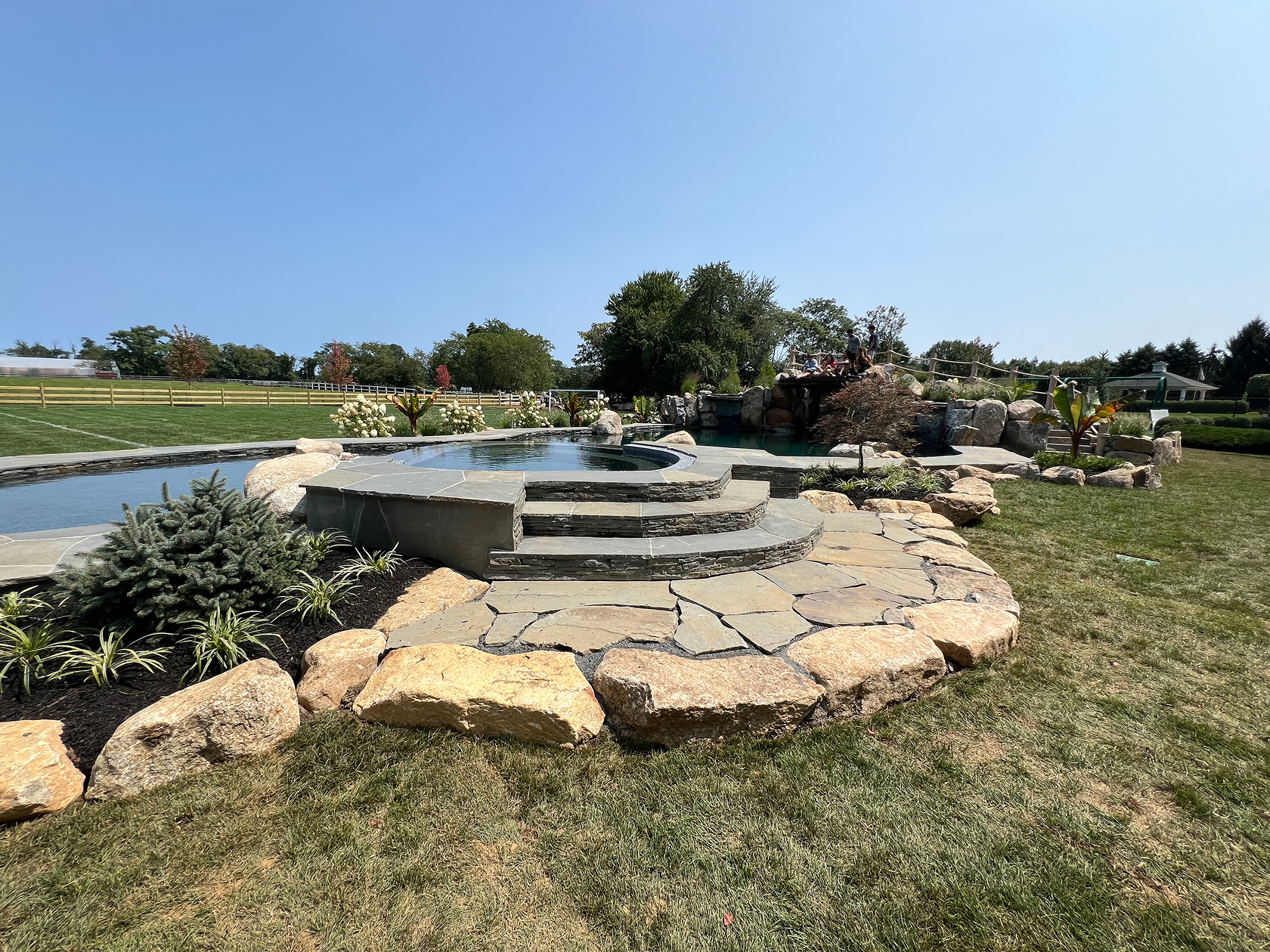 Wide view of grotto pool with sun shelf, stone spa and rock waterfalls, Colts Neck, NJ.