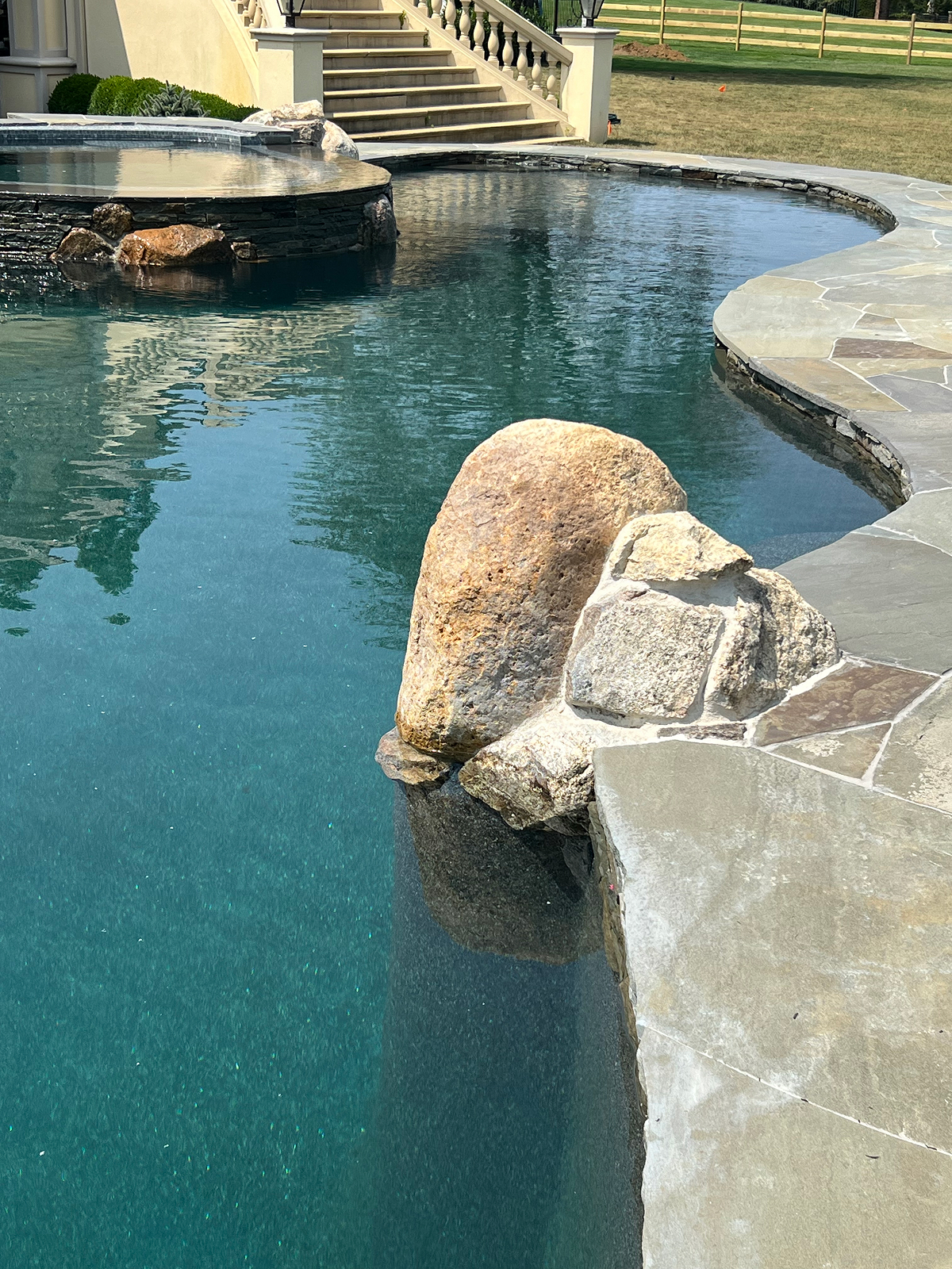 Evening view across pool toward waterfall grotto and stone boulders in Colts Neck, NJ.