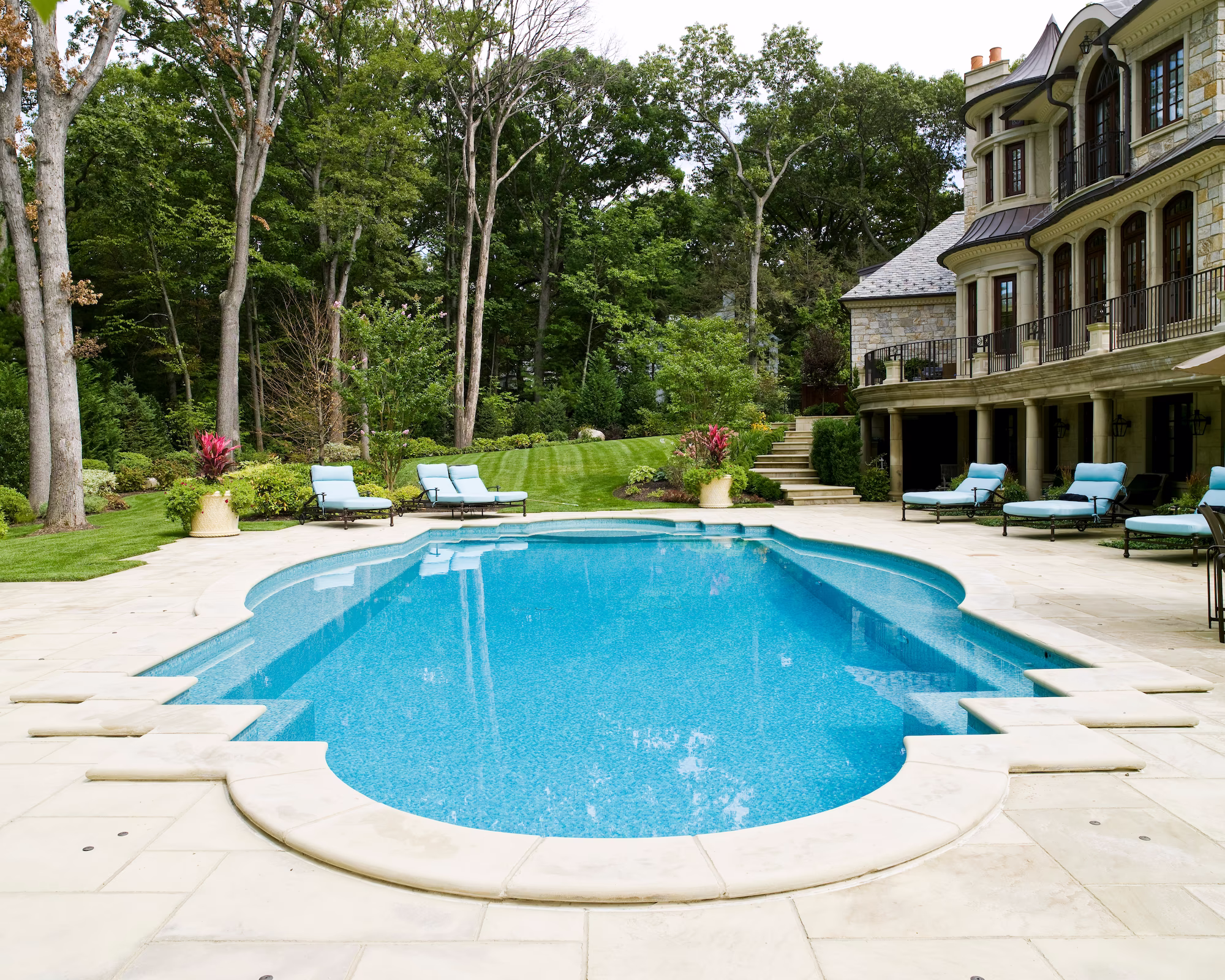 Wide backyard view of sculptural pool edge with custom mount coping, Essex Fells, NJWhispering Manor luxury pool with limestone coping and sun shelf, set against wooded grounds in Essex Fells, New Jersey