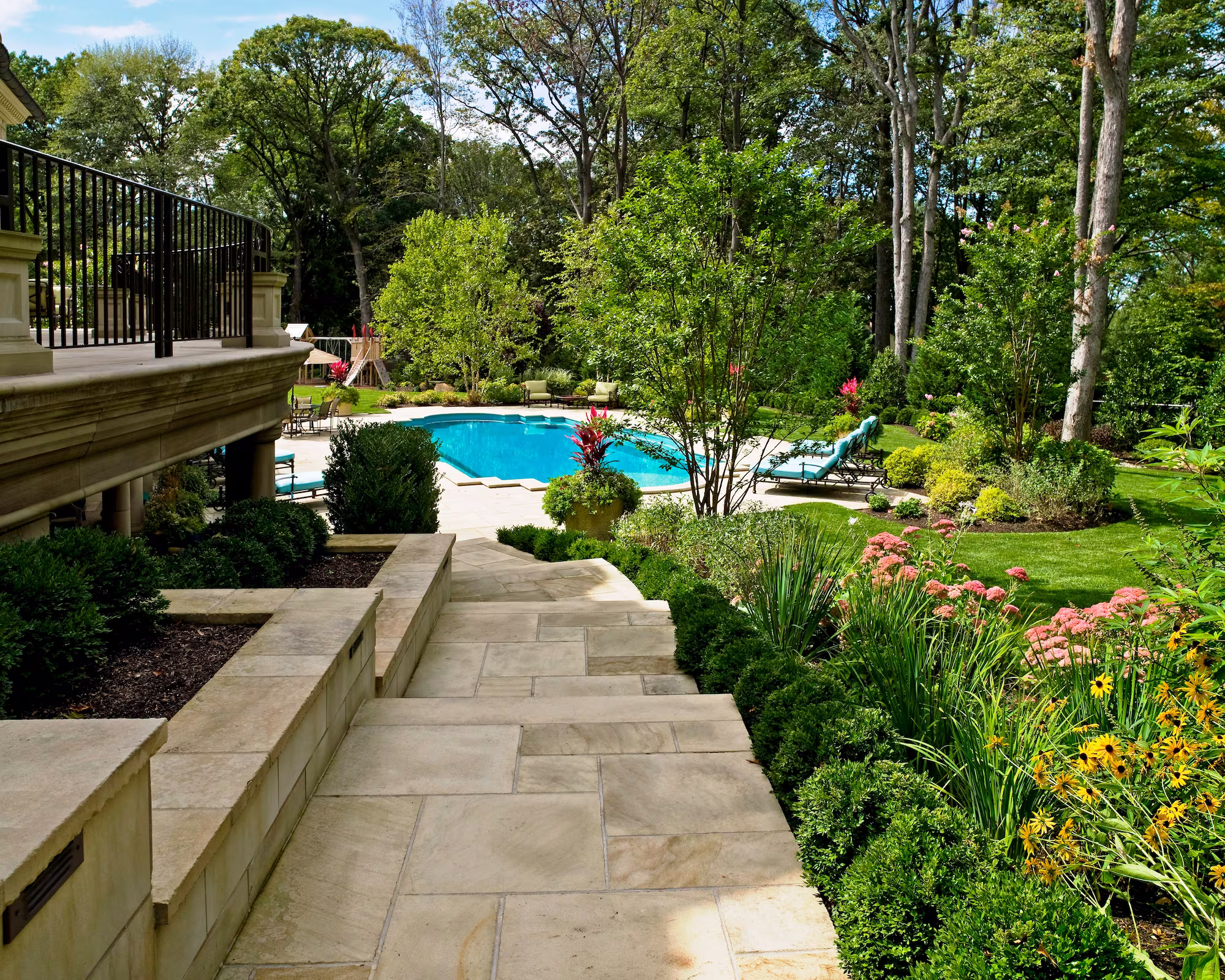Stone terrace steps descending to landscaped luxury pool and gardens at Whispering Manor in Essex Fells, NJ