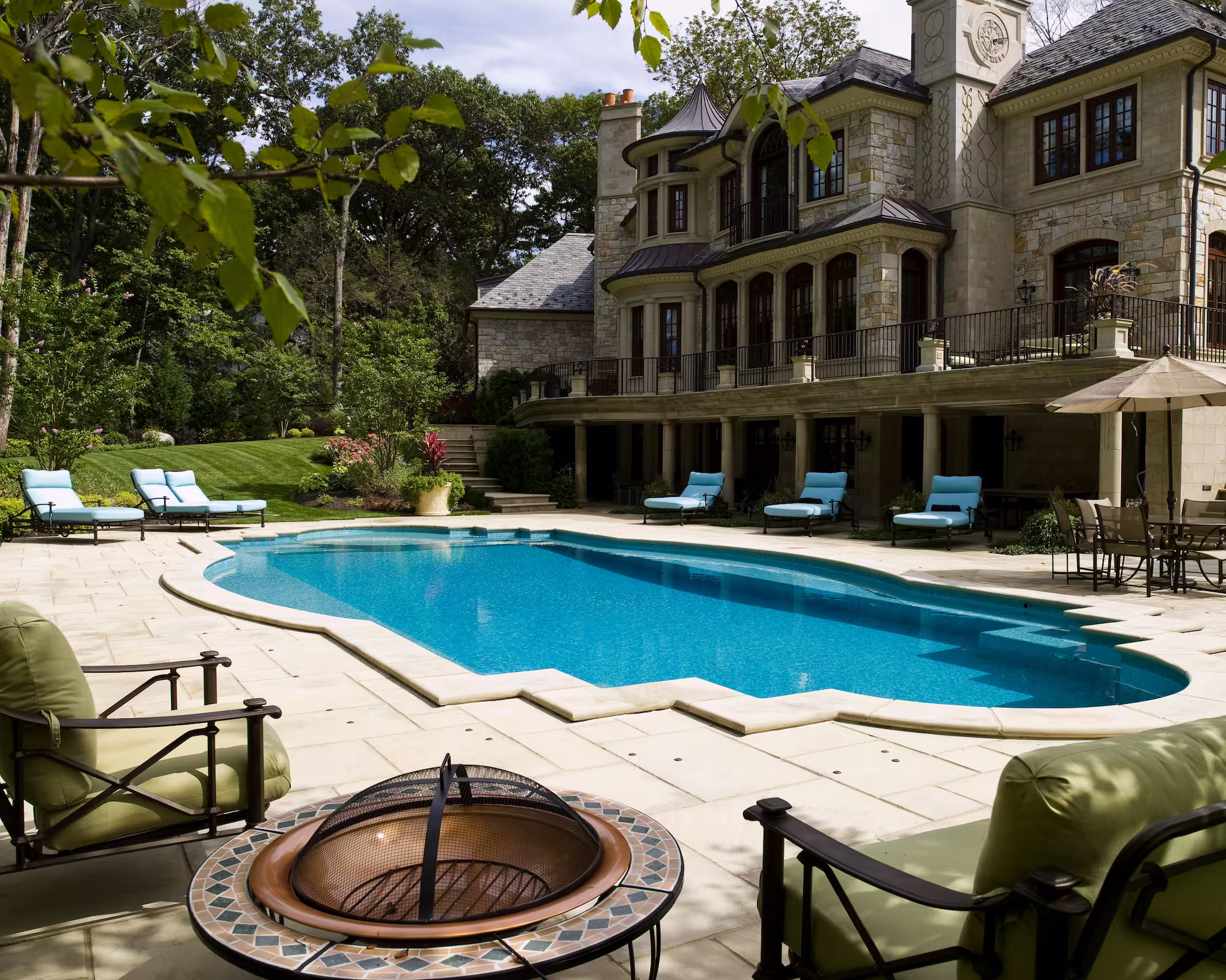 Circular fire pit seating area with view across the luxury pool to the residence at Whispering Manor, Essex Fells, NJ