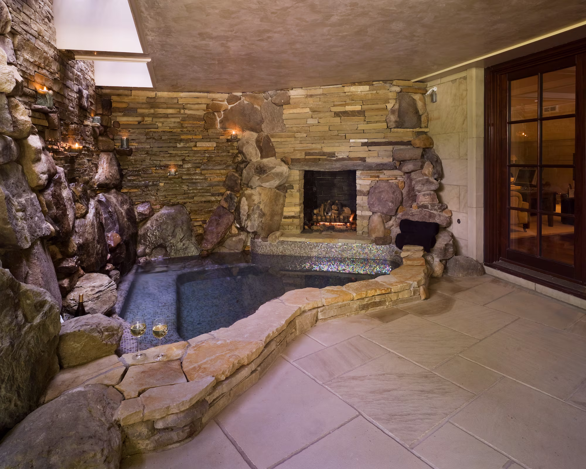 Indoor spa with natural rock waterfall and fireplace creating a grotto retreat at Whispering Manor, Essex Fells, NJ