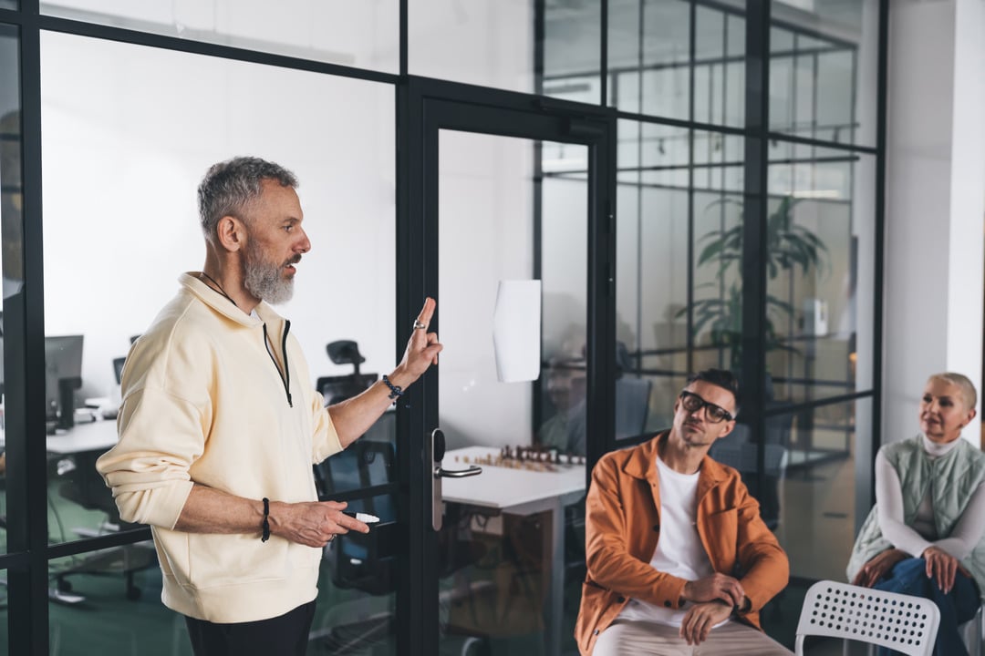 A person giving a presentation in a modern office while two colleagues listen attentively.