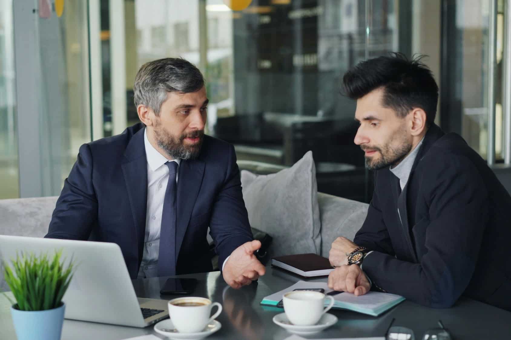 Two professionals engaged in a business discussion over coffee in a modern office setting.