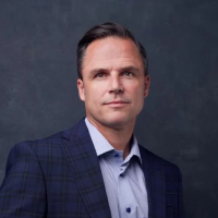 Professional man in a blue checkered blazer and light blue shirt against a dark gray background.