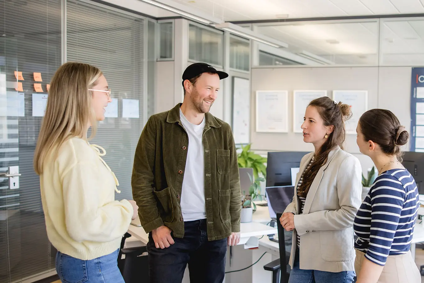 Vier Mitarbeitende von exporto tauschen sich in einem offenen Büro persönlich aus. Sie stehen in einer kleinen Gruppe zwischen Arbeitsplätzen und sprechen in lockerer, kollegialer Atmosphäre.