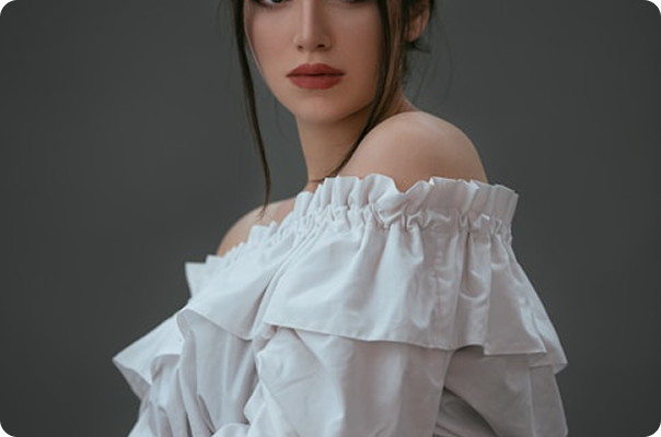 Woman in white ruffled off-shoulder top against gray background