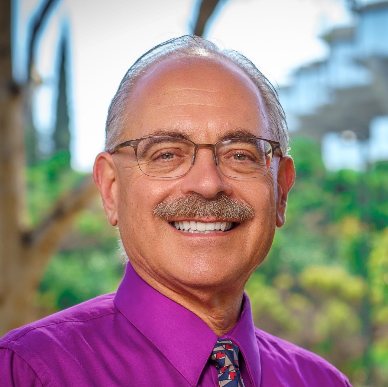 Smiling older professional in purple shirt and glasses outdoors