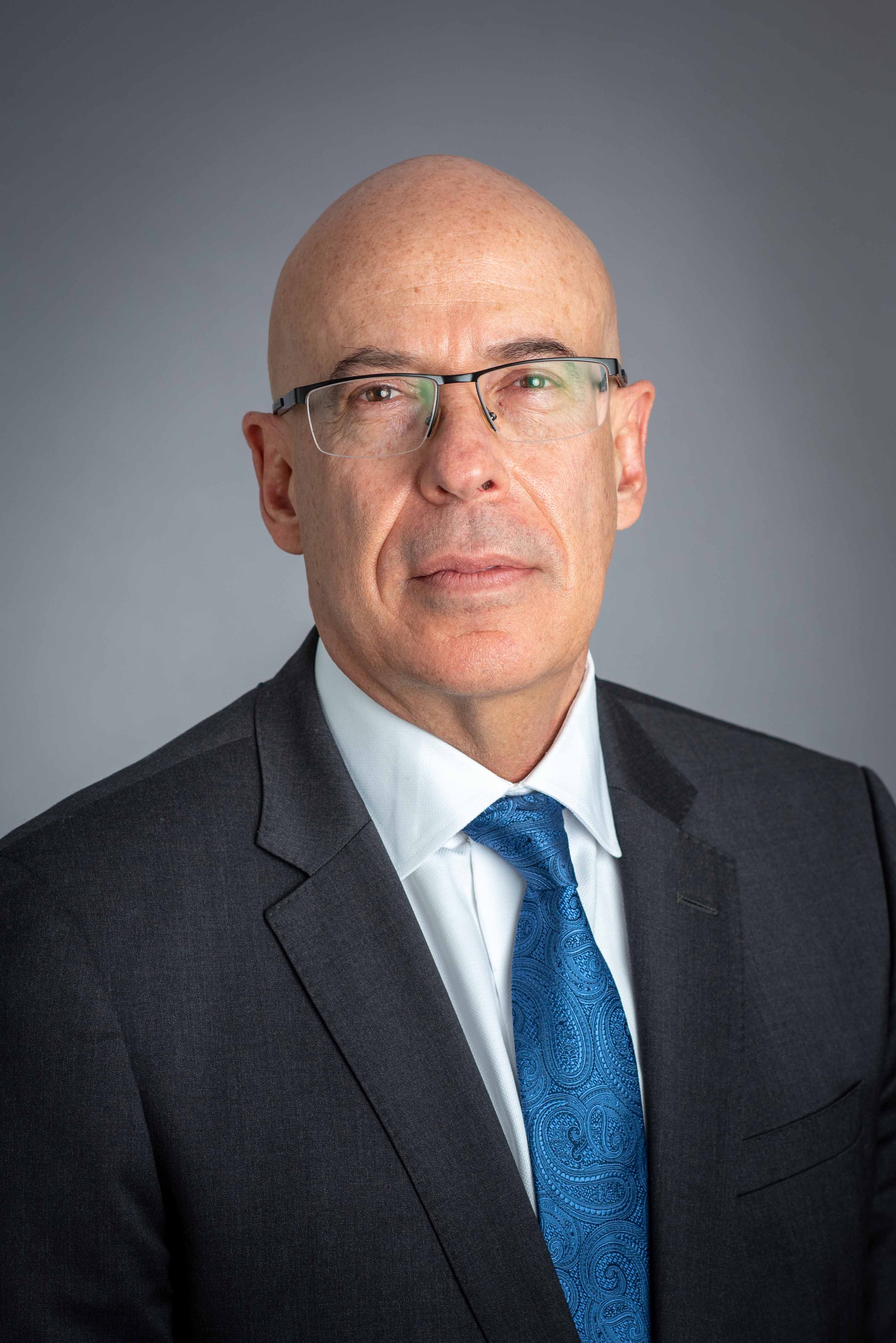 Bald professional in glasses and dark suit with blue paisley tie