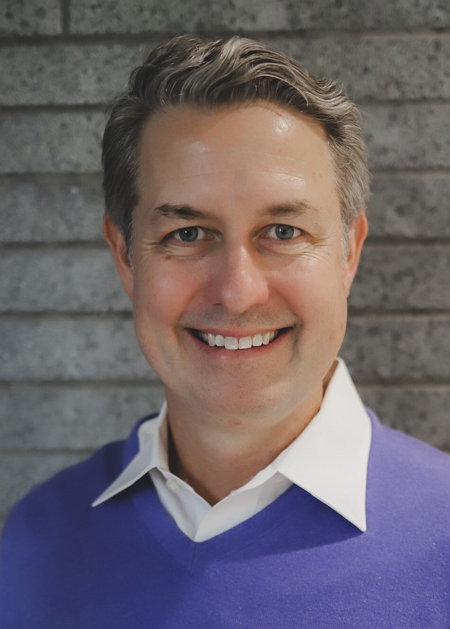 Smiling professional in blue sweater against brick wall background