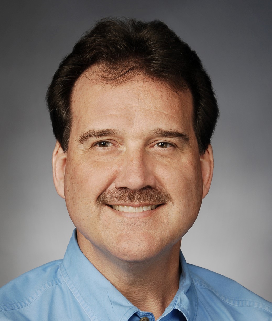 Middle-aged man with mustache smiling in blue shirt against gray background