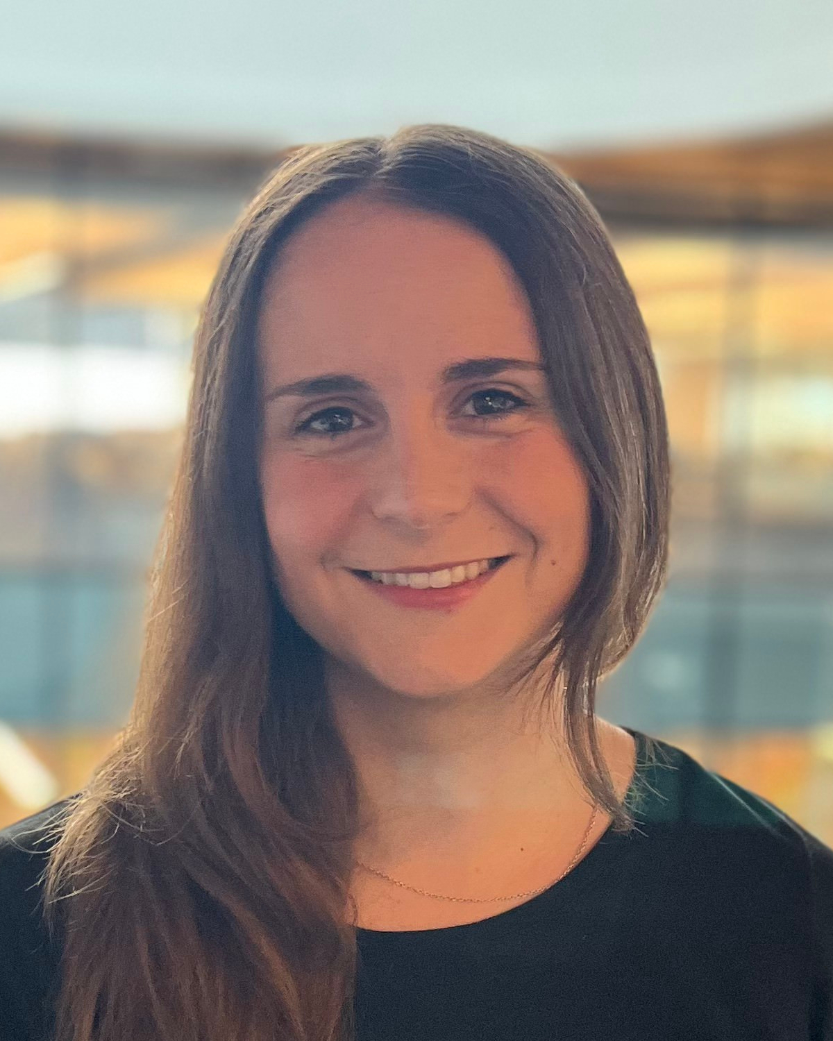 Smiling person with long hair wearing black shirt at sunset