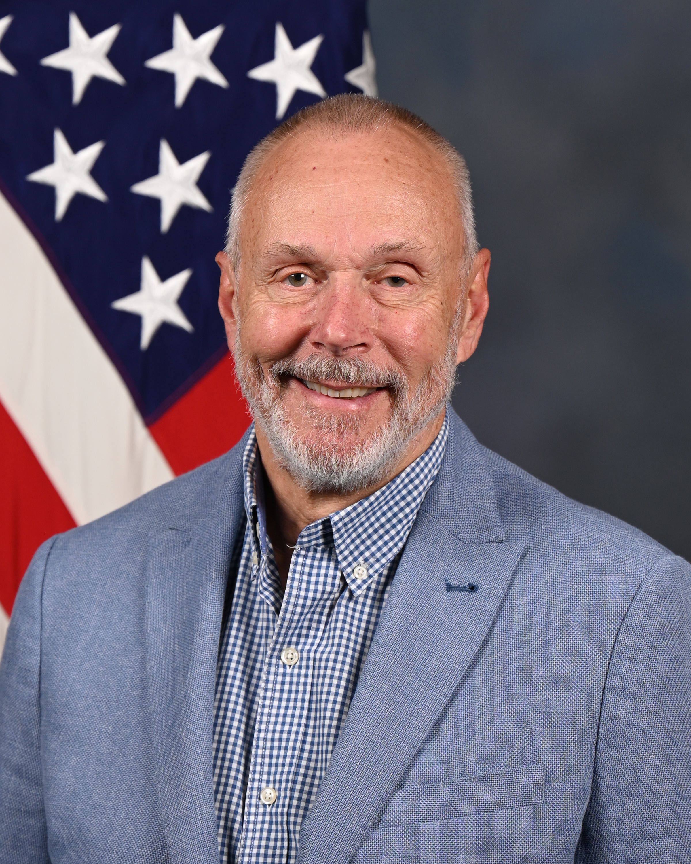Smiling older man in blue blazer posing in front of American flag