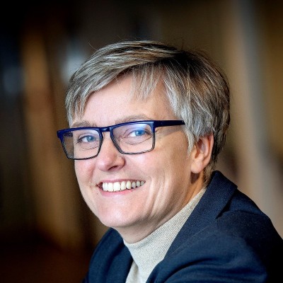 Smiling professional with short gray hair and blue glasses in navy jacket