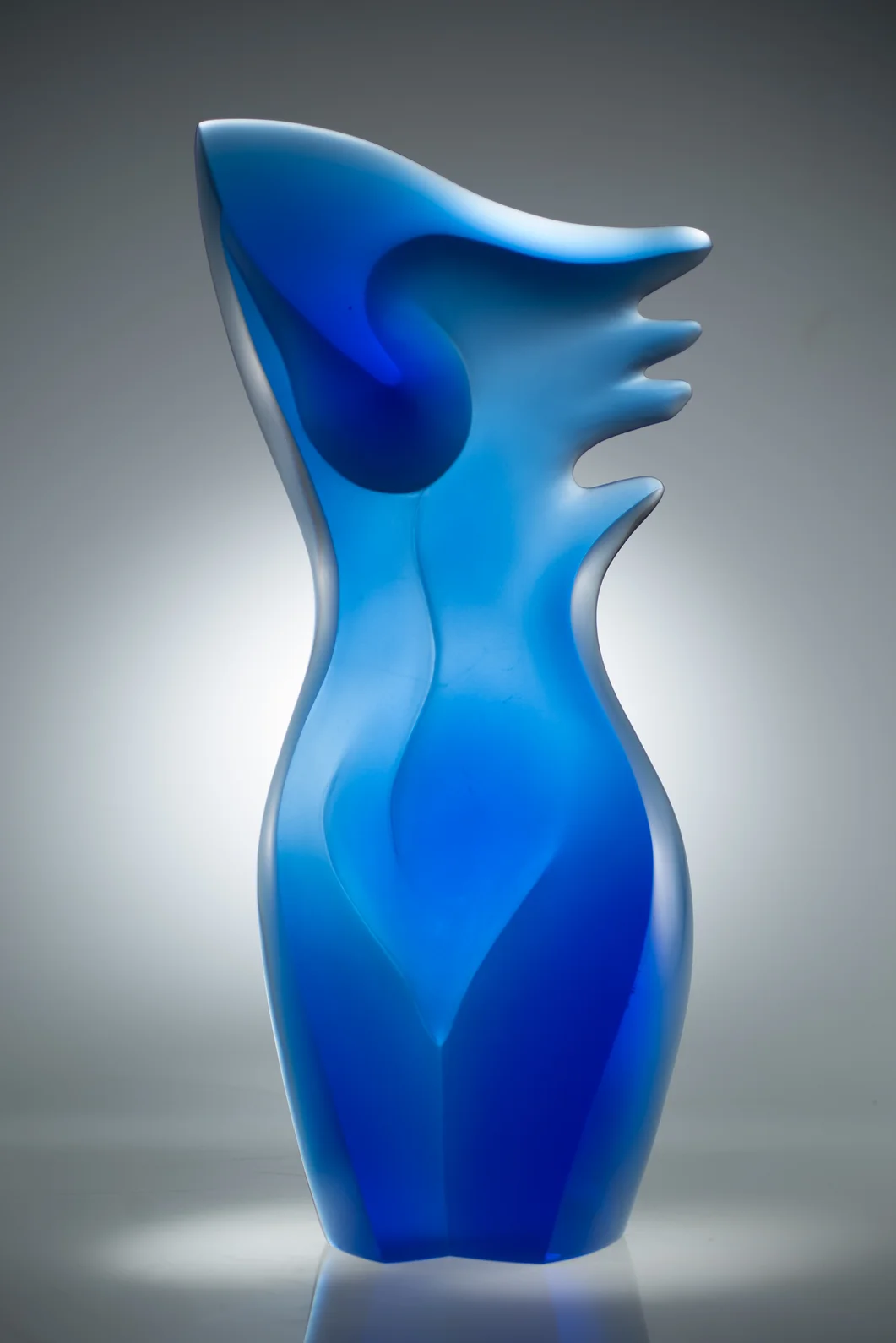 Blue glass sculpture with flowing lines in white gallery

