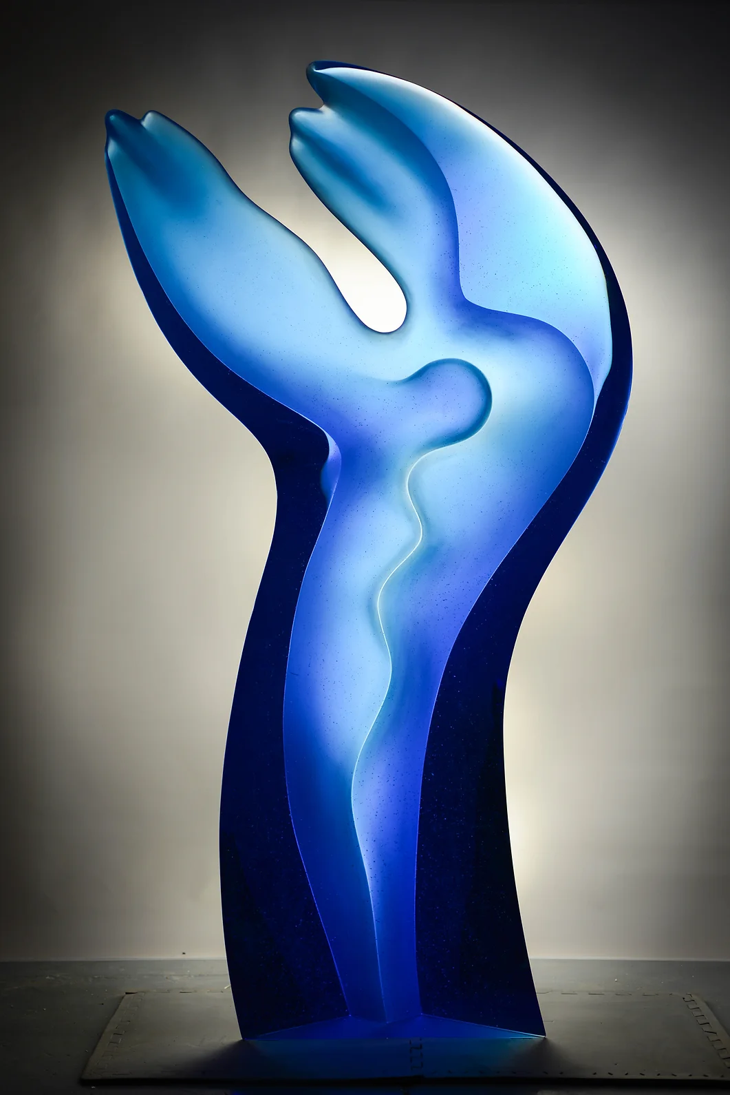 Blue glass sculpture with arms raised, lit from left