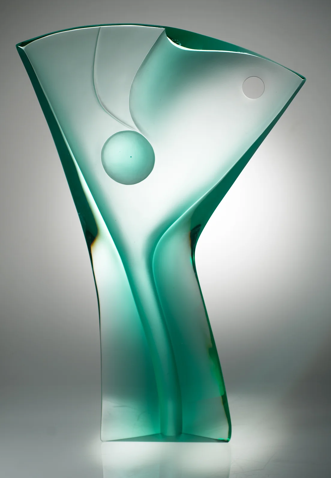 Green glass sculpture in spotlighted white space

