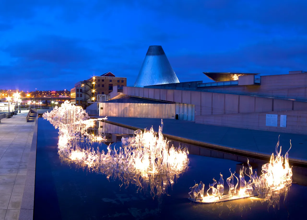 Illuminated glass sculpture floating on water outside the Museum of Glass during blue hour in Seattle.