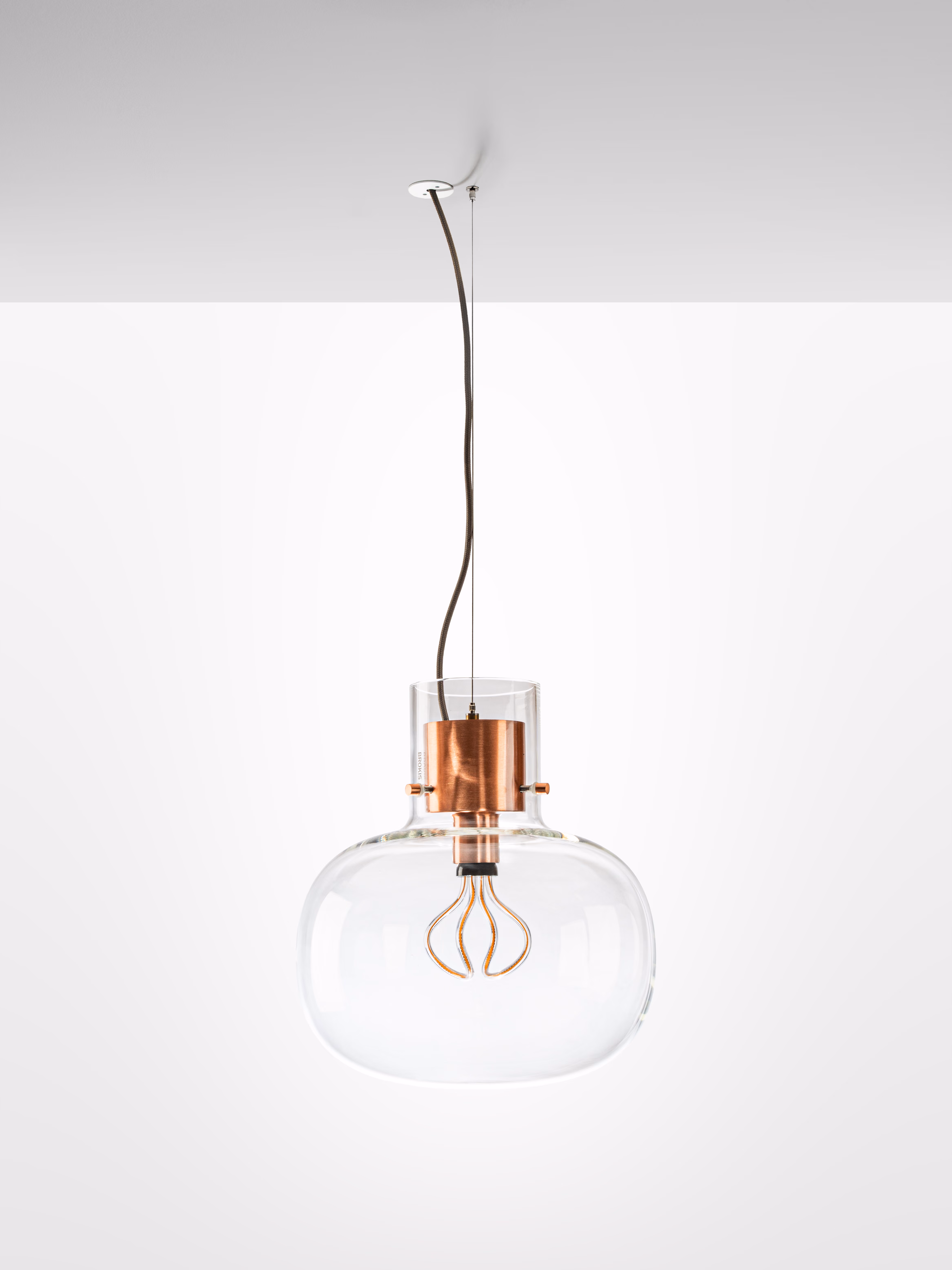 Modern pendant light with clear glass shade and copper fixture hanging from ceiling.