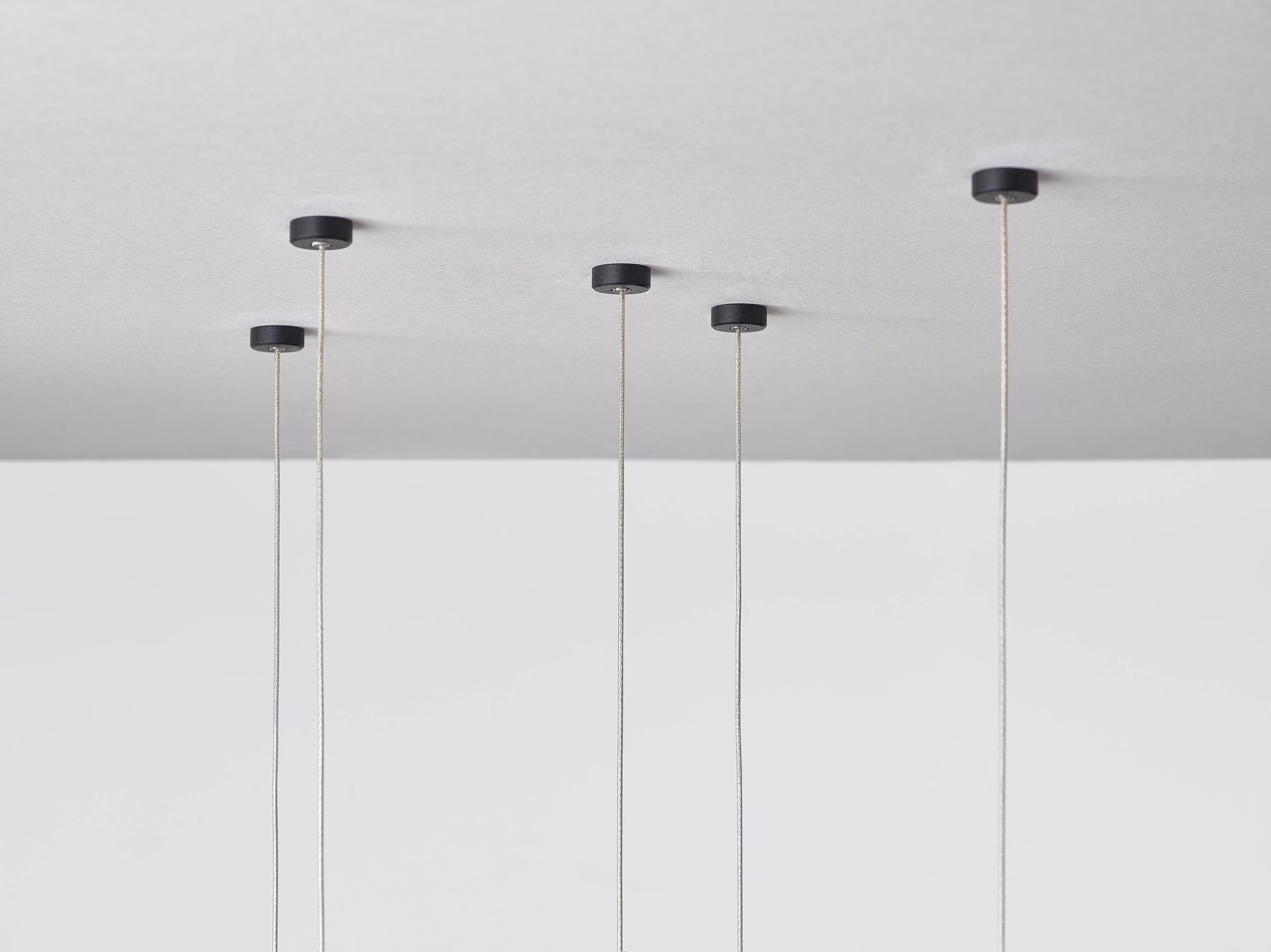 Five slim pendant light cords hanging from a ceiling with black mounts.