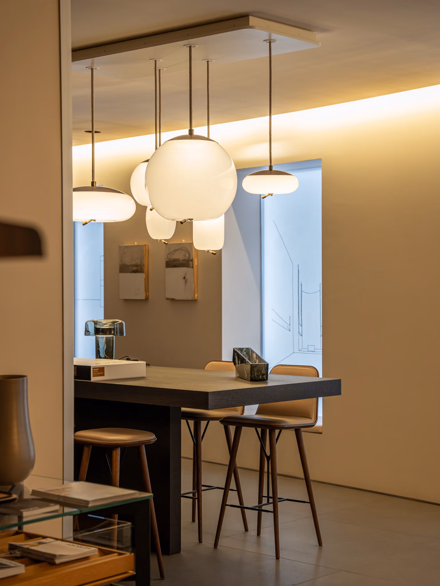 Modern dining area with hanging white glass pendant lights and tall wooden chairs around a dark table.