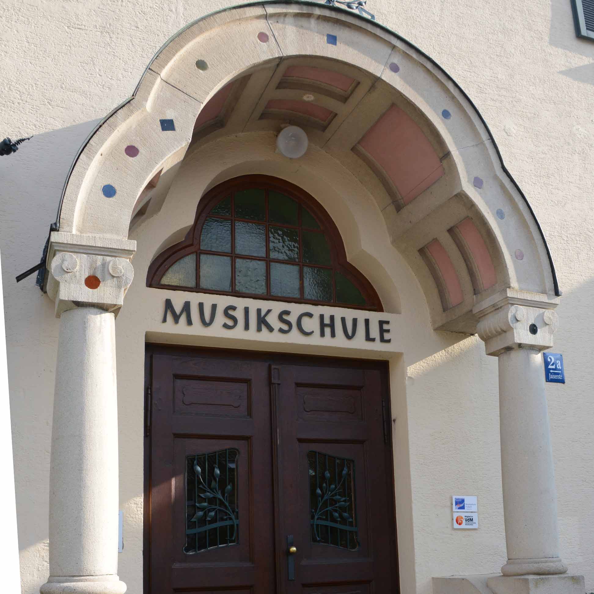 Eingangstür der Musikschule mit zwei Säulen und einem Bogen, darüber Schriftzug 'Musikschule'.