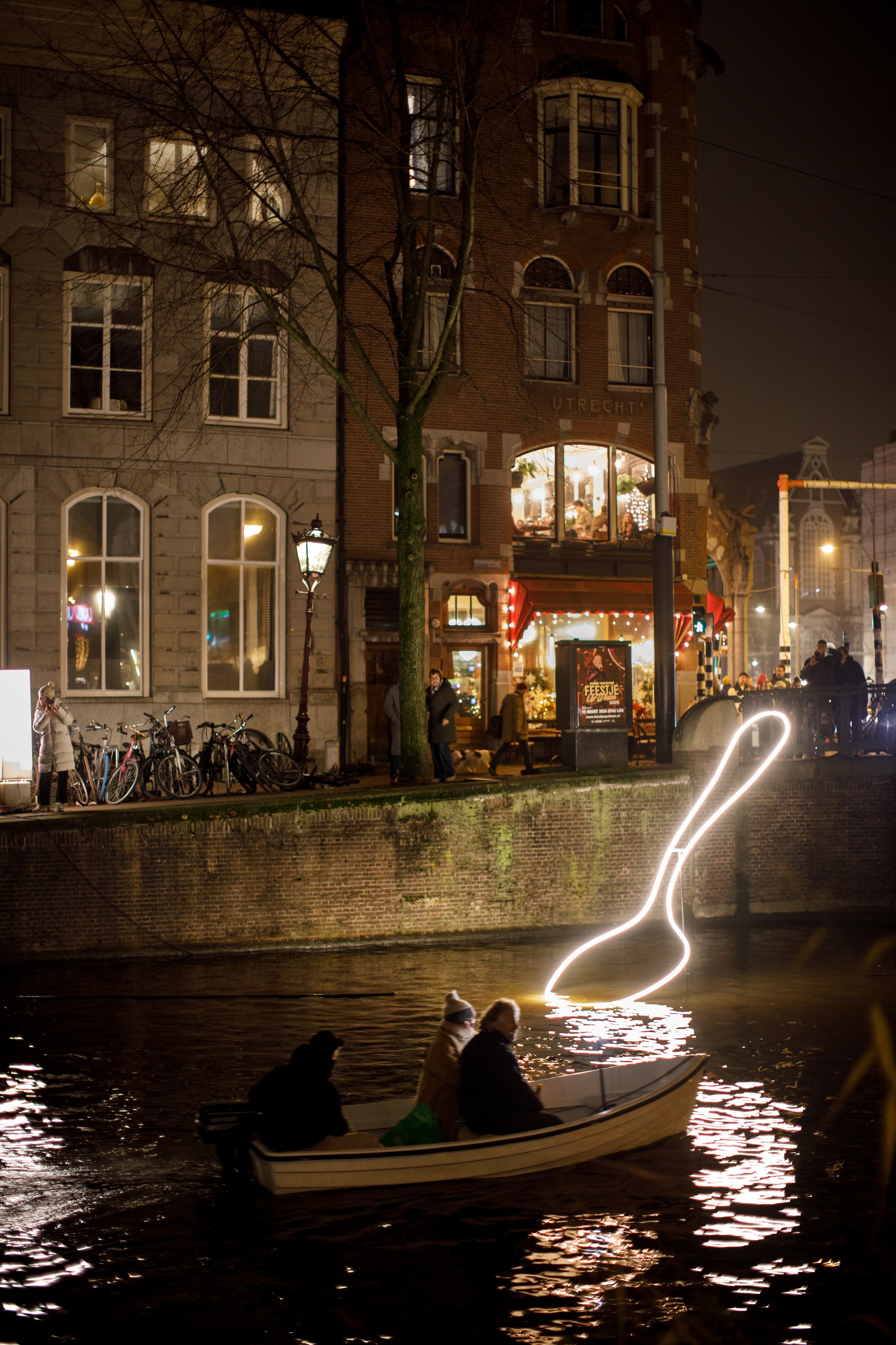 A portrait photograph of an illuminated spoon artwork resting in a canal at night.