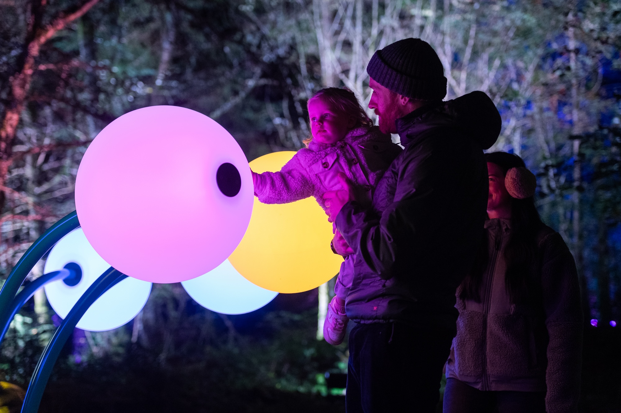 A man and child interact with a glowing bulb in the inBloom light installation