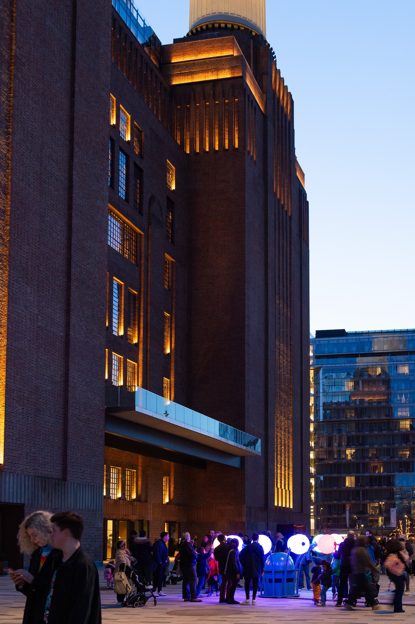 A light installation with bulbs that stem outwards like a flower from a central point, situated in front of battersea power station viewed from further away