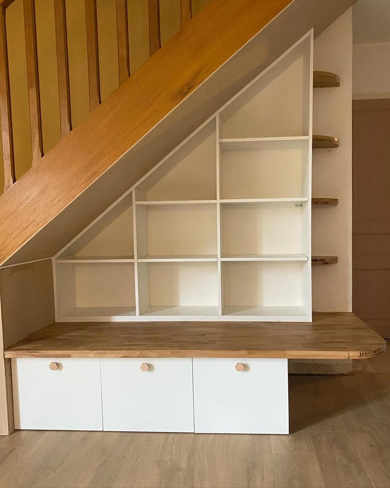 Meuble en bois sous escalier avec étagères et rangements.