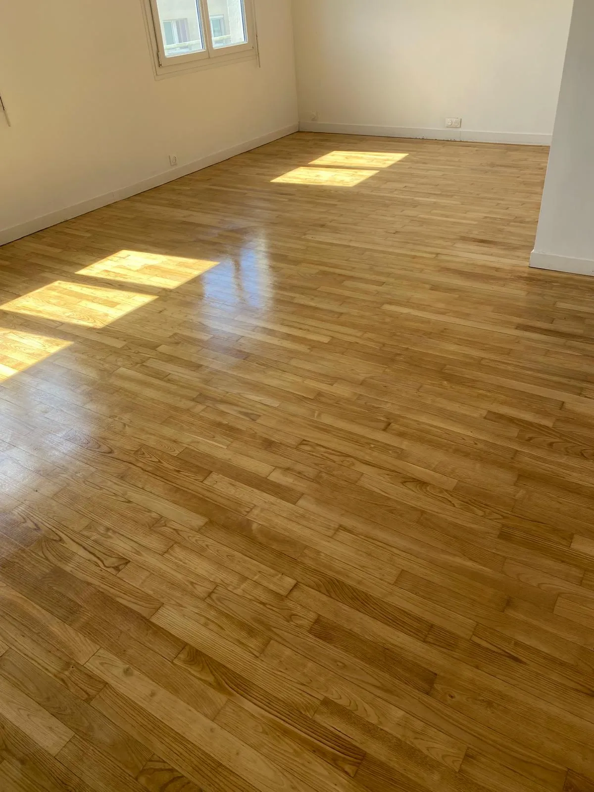 Parquet en bois clair dans une pièce vide et lumineuse.