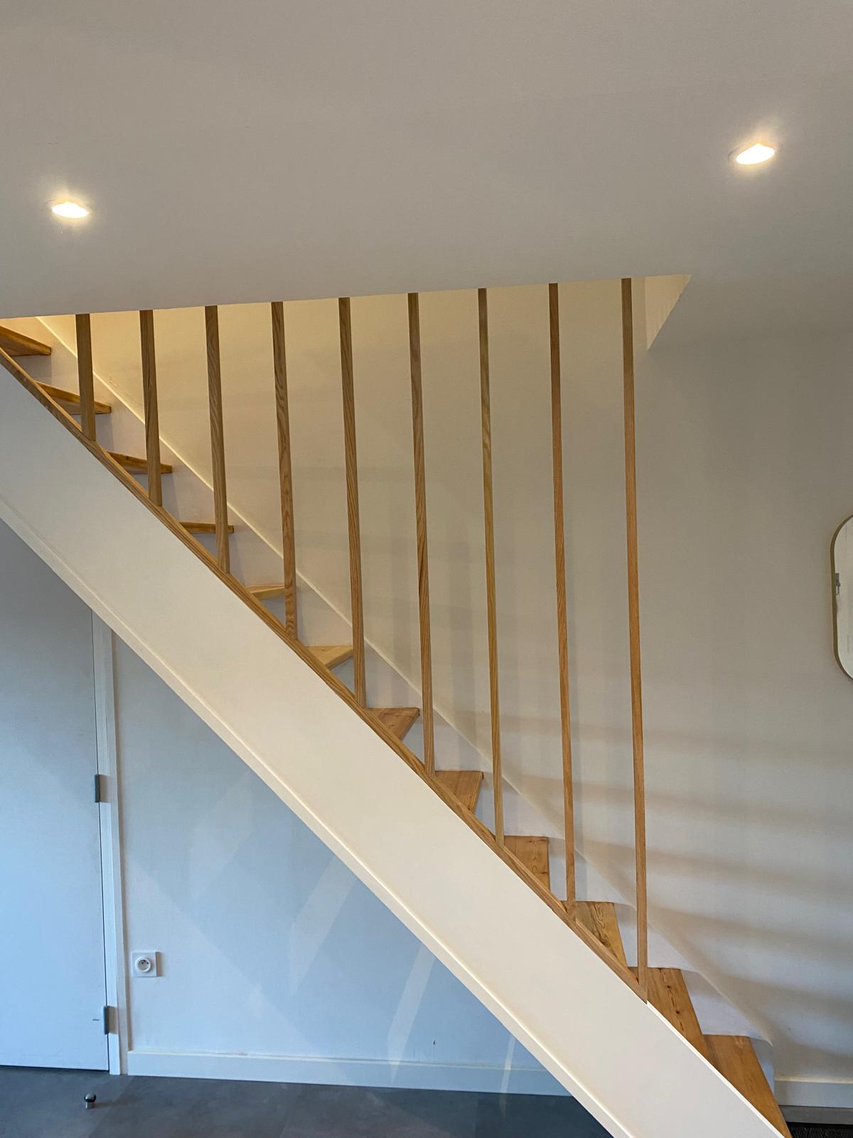 Escalier moderne avec marches en bois et garde-corps à barreaux verticaux.