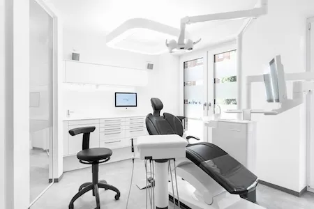 Moderne, helle Zahnarztpraxis mit Behandlungsstuhl, Hocker und zahnärztlicher Ausrüstung.