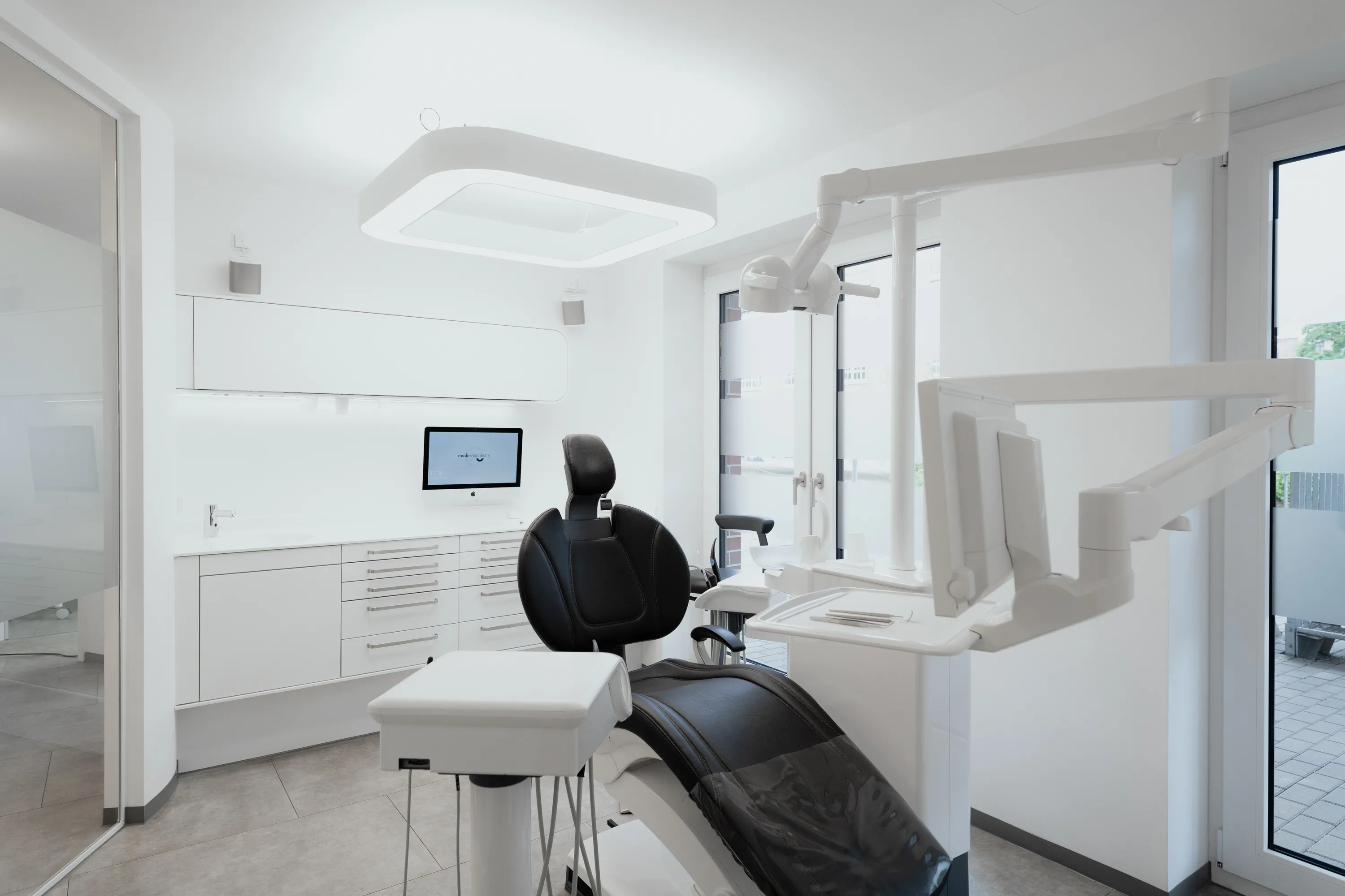 Moderne Zahnarztpraxis mit schwarzem Behandlungsstuhl, weißem Arbeitsbereich und Monitor an der Wand.