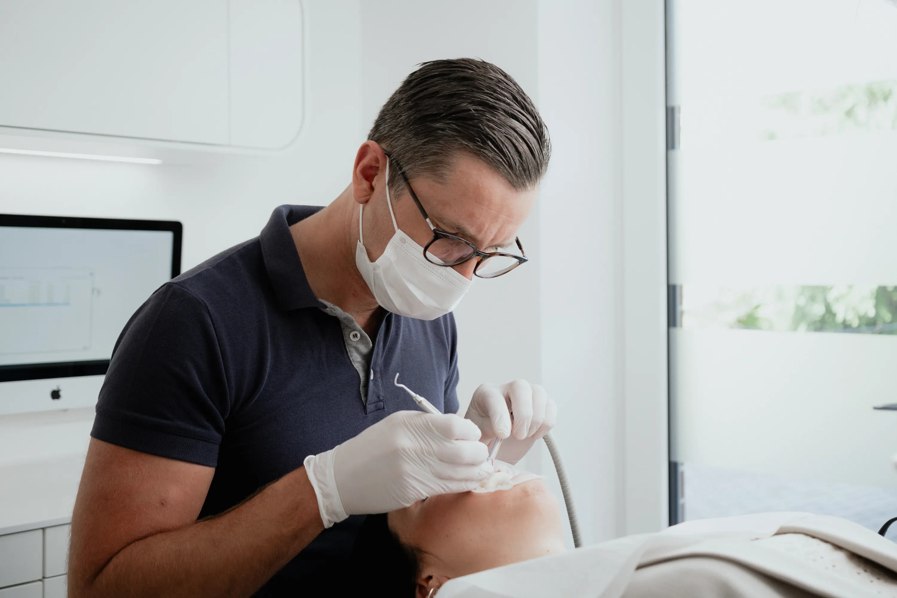 Zahnarzt Dr. Niels Hoffmann behandelt Patientin bei einer Paradontits Behandlung mit Handschuhen und Maske in moderner Praxis.