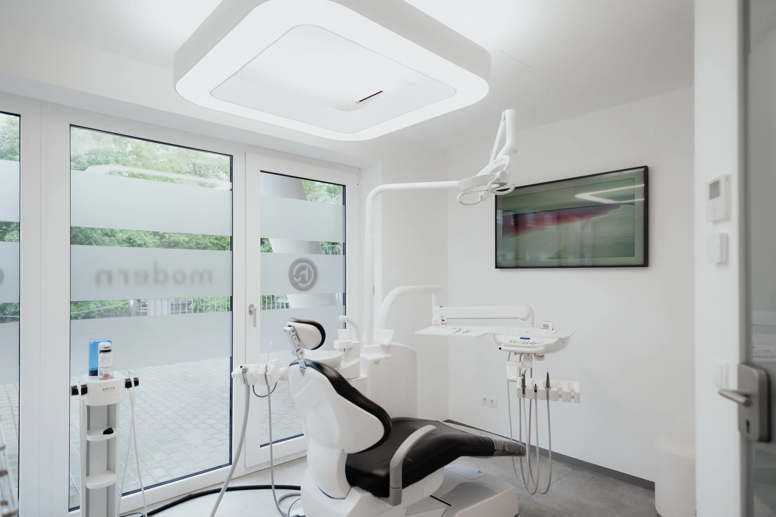 Moderner, heller Zahnarztbehandlungsraum mit schwarzem und weißem Behandlungsstuhl und großem Fenster.