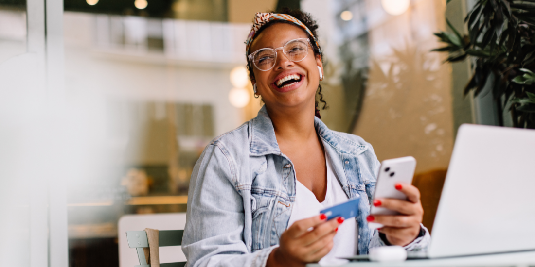 A customer smiles while holding a credit card in one hand and their cell phone in another.