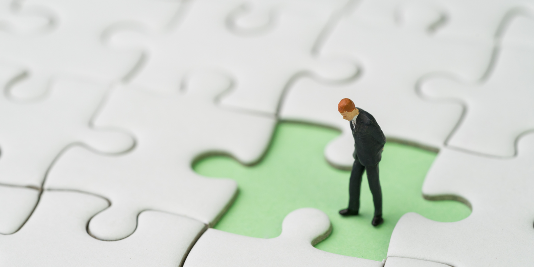 A close-up of a toy human figurine pondering a missing piece in the middle of a puzzle.