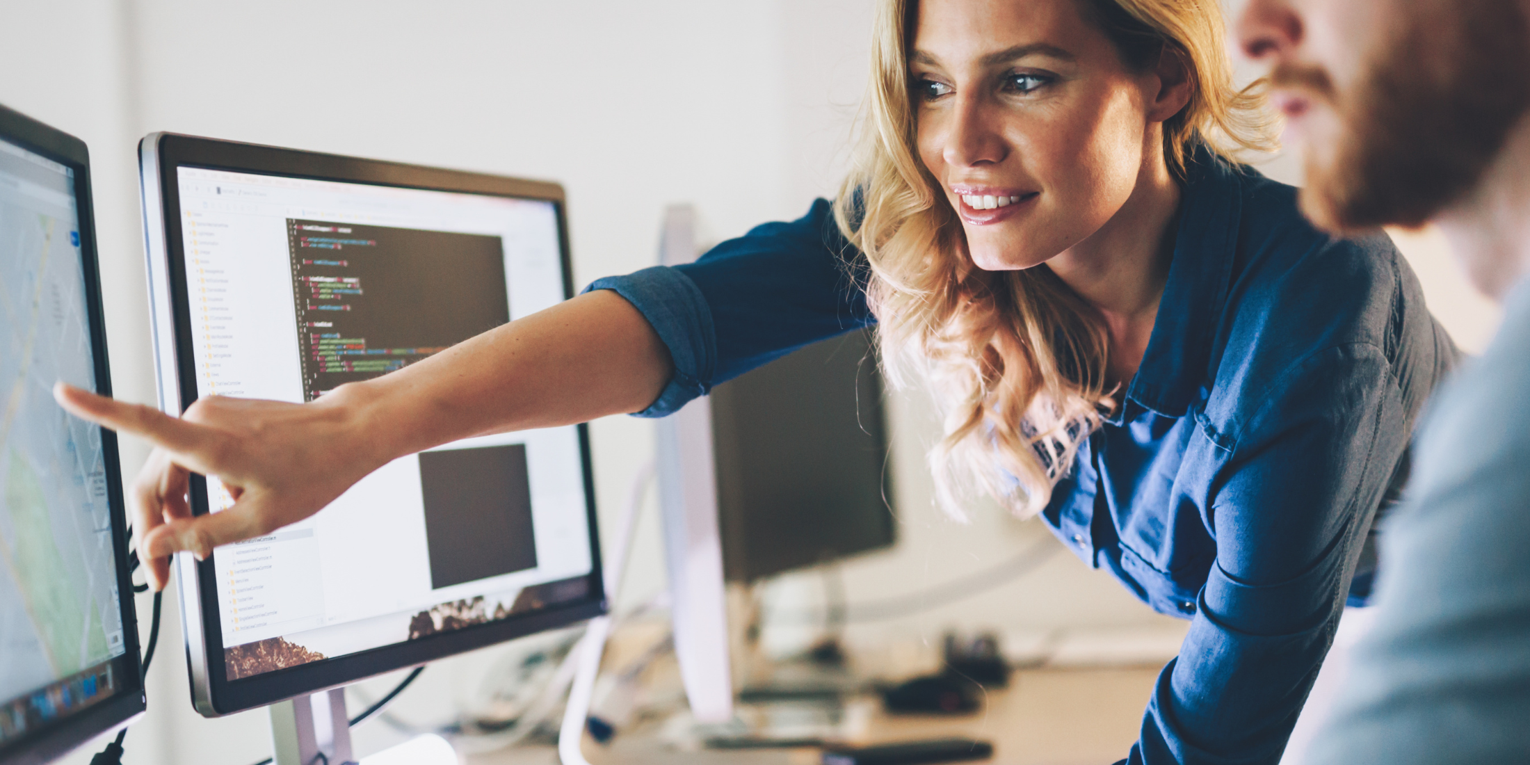 Blonde woman pointing at computer screen with blurry man in foreground