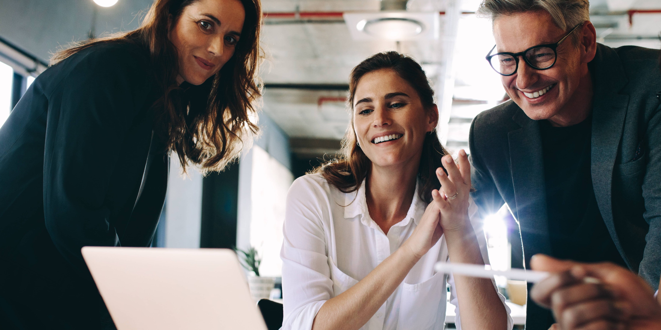 Two women, one man smiling and looking at computer