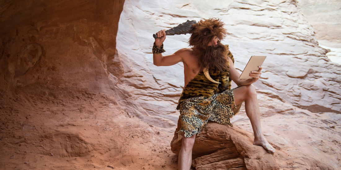 Caveman scratching his head with a club while looking at his stone tablet outdoors in a weathered rock cave